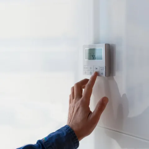 Hand adjusting a wall-mounted thermostat.